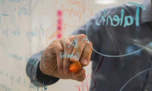 person writing on glass whiteboard with diagrams